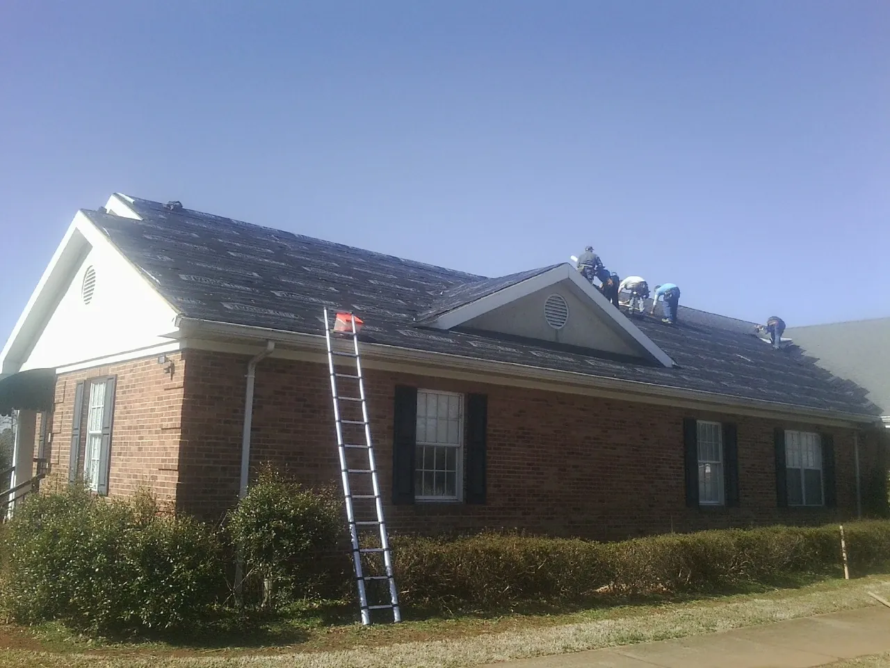 Crew tearing shingles off a brick ranch roof with a ladder set — Metal Roof Repair work by our crew in Chester Gap