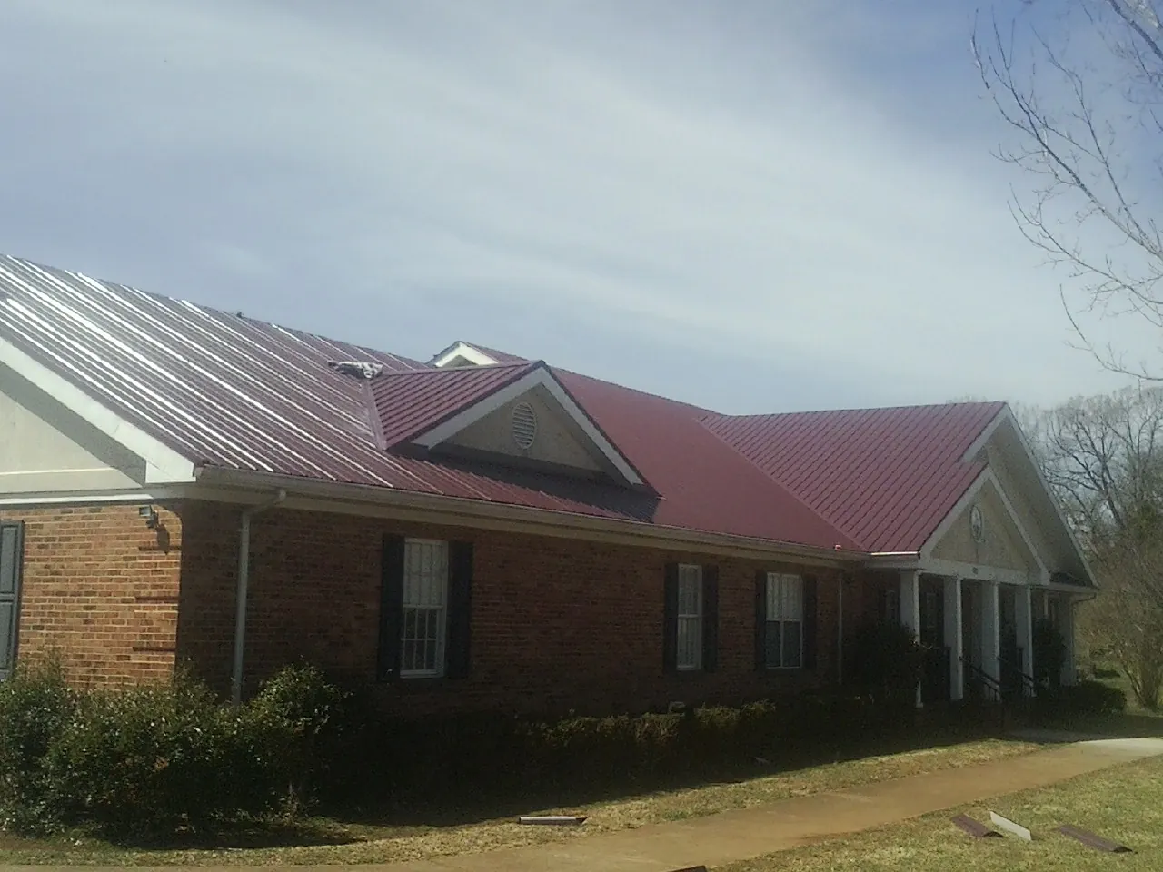 Red metal roof with gabled entries on a long brick building, from a Hail Damage Roof Repair job in Chester Gap