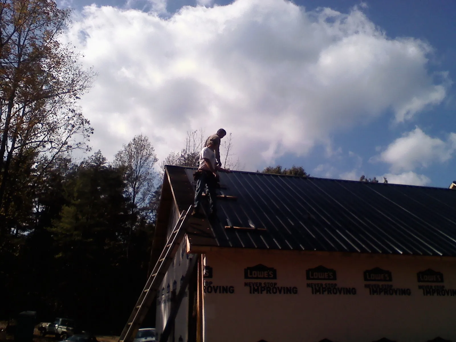 Roofer fastening dark metal panels high against a cloudy sky, from a Roof Inspection job in Chester Gap