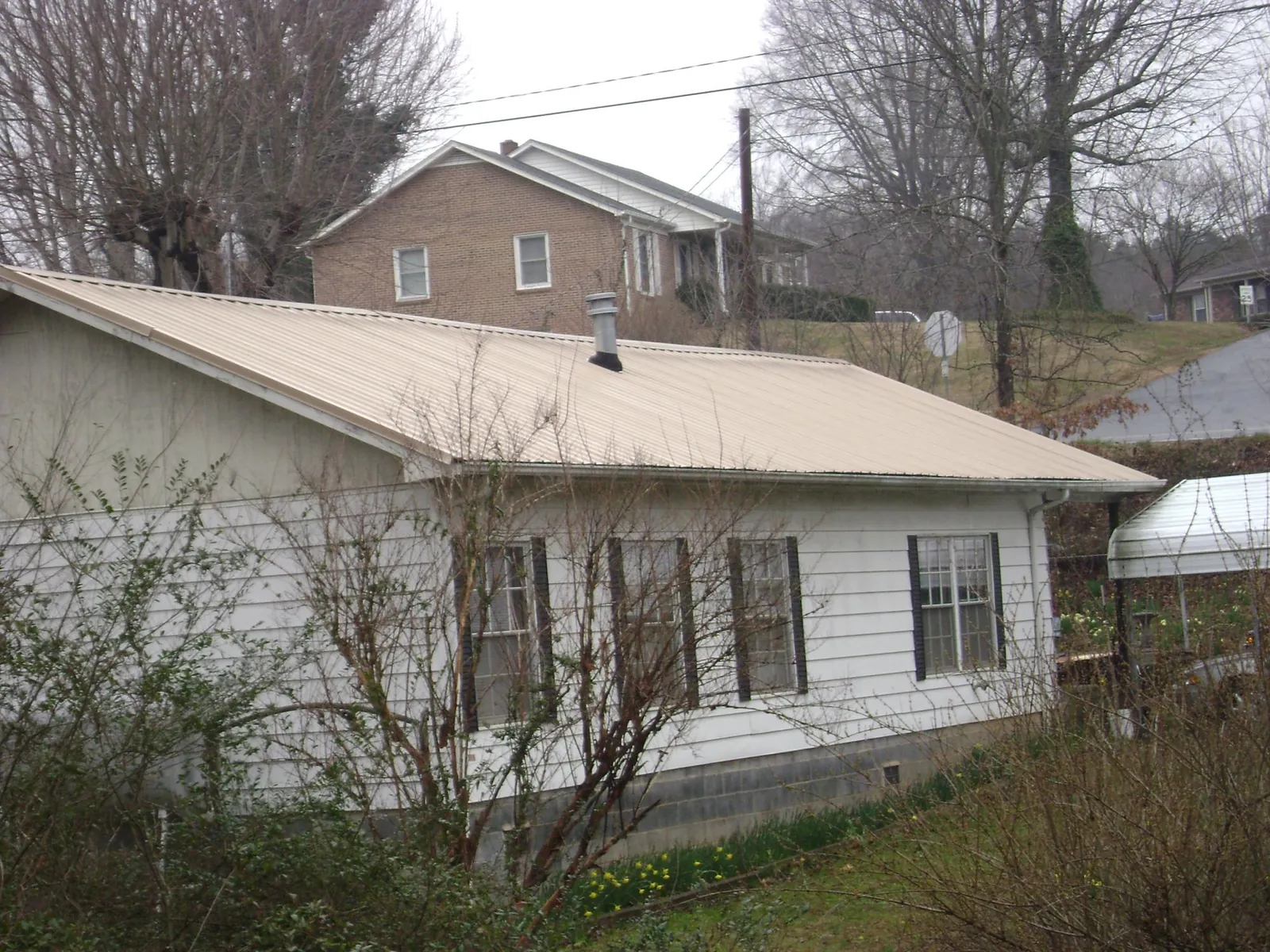 Tan metal roof on a white sided house set into a hillside — Commercial Roofing by Roofing Brothers in Chester Gap